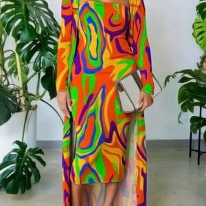 Indoors, a person holds a clutch and wears the Multi Color 2 Piece Strapless Dress and Cardigan. Large green plants are visible in the background.