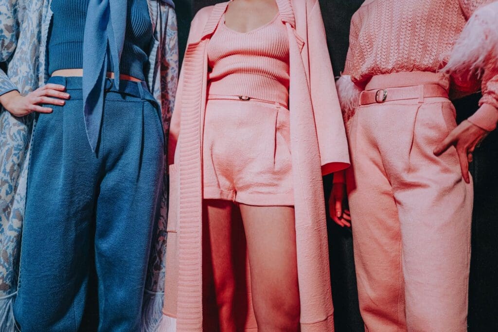 Three people stand side by side, each wearing stylish, textured outfits in shades of blue and pink, with the photo showing them from shoulders to knees.
