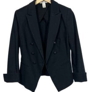 The (WHBM) Blk Dbl Breast Jacket, featuring a black double-breasted design with three front buttons, hangs on a wooden hanger against a white background.