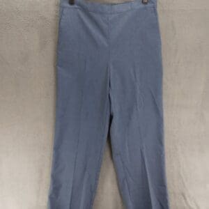 A pair of blue dress pants hangs on a black plastic hanger against a light gray fabric background.