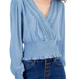 Woman wearing a light blue, long-sleeve blouse with lace detailing, a smocked waist, and high-waisted blue jeans with buttons.