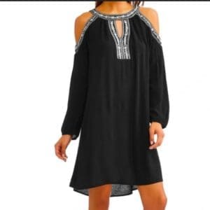 A woman wears a black, knee-length, cold shoulder dress with long sleeves and decorative white embroidery along the neckline and shoulders.