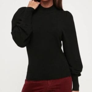 A person wearing a black long-sleeve sweater with puffed shoulders and burgundy pants, posed against a plain white background.