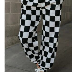 Person wearing black and white checkered pants and white sneakers, standing on a concrete sidewalk with hands in pockets.