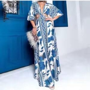 A person wearing a long, blue and white patterned dress stands near a bright blue door, holding a beige feathered clutch.