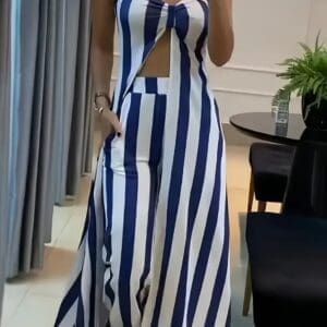 Person wearing a strapless jumpsuit with vertical blue and white stripes, a front cutout, and wide-leg pants, standing indoors near furniture and a plant.