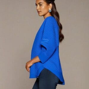 A woman in a Blue Quilted Top with Pocket Sleeve and dark jeans stands in profile against a plain background.