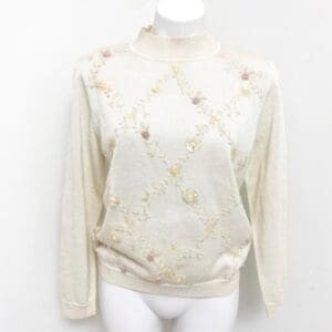 Cream-colored long-sleeve sweater with a mock neck, featuring a subtle floral pattern and sequins arranged in a diamond grid on the front.