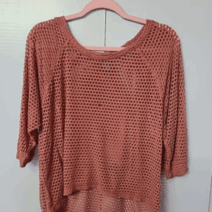 The Bobeau Dark Salmon Holy Top is a loose, crochet-knit top with three-quarter sleeves, shown hanging on a pink hanger against a light gray background.