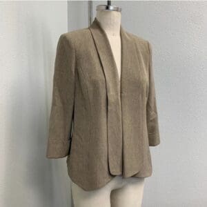 Tan women's blazer with an open front, long sleeves, and a tailored fit displayed on a dress form against a plain light-colored wall.