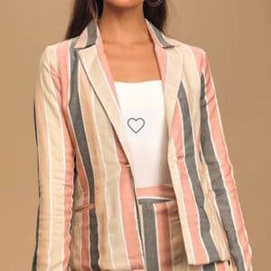 A woman wearing a pastel striped blazer and matching pants over a white top, standing against a plain beige background.
