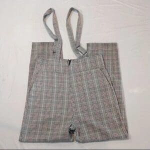 Plaid overall shorts with suspenders laid flat on a white surface.