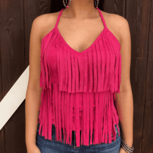 A woman stands against a dark wooden background wearing a Hot Pink Suede Fringe Tank Top, blue jeans, large hoop earrings, and bracelets.