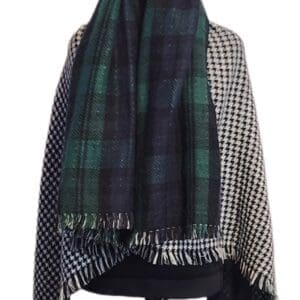 A mannequin displays a shawl with one side in black and white houndstooth pattern and the other in green and black plaid, featuring fringed edges.