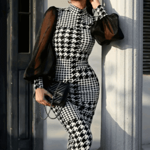 Woman in a Black & White Checkered Sheer Sleeve Dress, holding a black purse and wearing dark sunglasses, stands by a column.