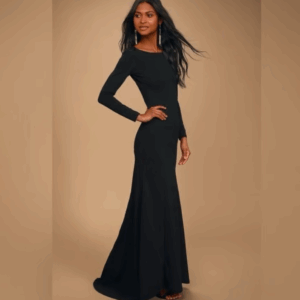 A woman stands on a neutral background wearing a long-sleeve, floor-length black gown with a fitted waist and flared hem.