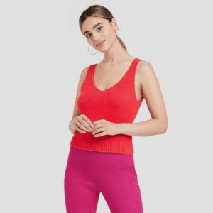 A woman wearing a red sleeveless top and high-waisted pink pants stands against a plain light background.