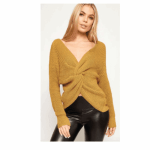 Woman wearing a mustard yellow knit sweater with a front twist detail and black leather-look pants, standing against a plain light background.