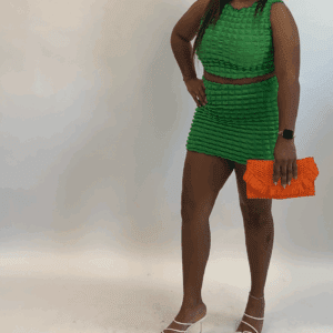 A woman wears the 2 PC Sleeveless Crop Top & Skirt in green, styled with an orange clutch, standing against a plain white background.