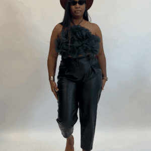 Woman in a sleeveless green top with ruffles, black leather pants, yellow shoes, burgundy hat, and sunglasses stands against a plain white background.