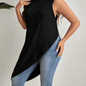 A woman models the Black Sleeveless Asymmetrical Top with light blue jeans, standing by a textured wall.