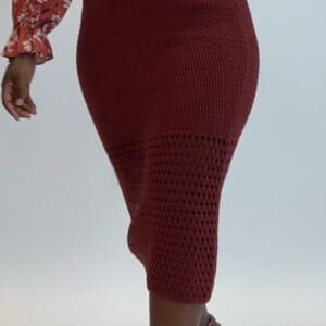 A person wearing a fitted, burgundy crocheted midi skirt and a floral long-sleeve top walks forward against a plain background.