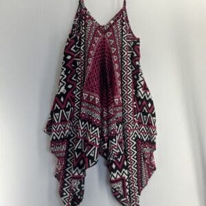 The Flowy Cami Top is a sleeveless piece with thin straps, a layered handkerchief hem, and a striking black, white, and magenta geometric pattern.