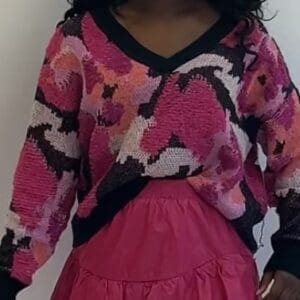 Model wears the Long Sleeve Shades of Pink Sweater, featuring loose fit in pink and black hues, paired with a bright pink skirt against a plain white background.