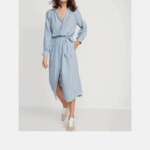 A woman wears the Long Striped Button Down Shirt Dress in light blue and white with beige sneakers, standing against a plain white background.