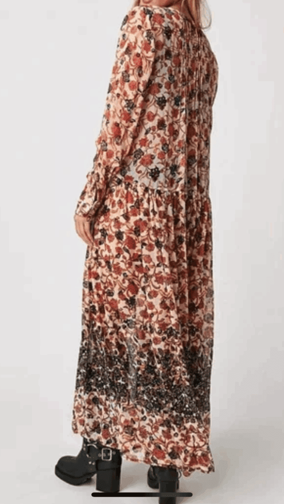 Model wears the Long, Long Sleeve Sheer Flowered Dress, an ankle-length floral piece with ruffled hem, paired with black boots; shown from the back against a plain background.