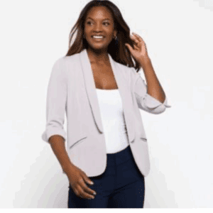 A woman smiles and touches her hair while wearing the Blazer over a white top and dark pants, standing against a plain background.