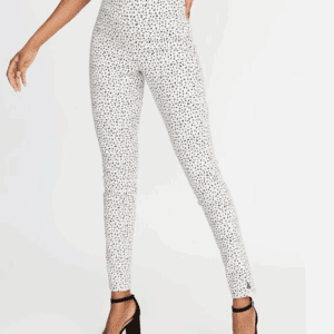 Woman wears Sheer Cover Up Pants—high-waisted, white with small black polka dots—paired with a black top and black heeled sandals. Only her lower body is visible.