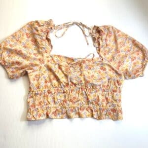 The Flowered Tie Back Crop Top features a cropped fit, short puffed sleeves, floral print, ruffled hem, and neck tie detail, shown laid flat on a white background.
