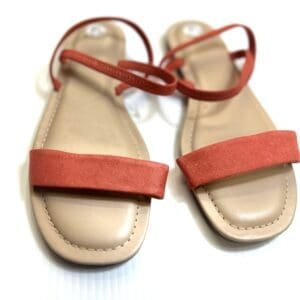 The Strappy Sandal, a pair of tan sandals with red suede straps and ankle ties, is displayed on a white surface.