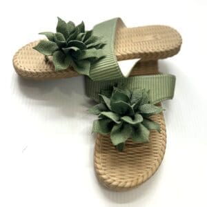 The Strappy Sandal features wide green woven straps, each topped with a fabric succulent, shown on a white background.