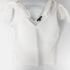 The White Tie Shoulder Top is a sleeveless V-neck with wide shoulder straps tied in bows, shown on a clear plastic hanger against a light background.