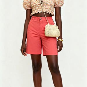 Model wearing a floral puff-sleeve crop top and coral Bermuda Shorts Size: 18 with a straw crossbody bag and white sandals.