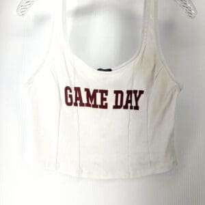 A white tank top with the words "GAME DAY" printed in bold red letters on the front, hanging on a clear plastic hanger.