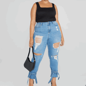 A person wearing a black sleeveless top, Denim Ripped Belted Ankle Jeans with tied hems, holding a black handbag, and wearing clear-strap heels.