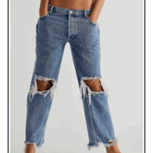 Model in Off the Shoulder Be Bold Top and high-waisted, light blue ripped jeans with frayed knee holes and raw hems, standing barefoot against a plain background.