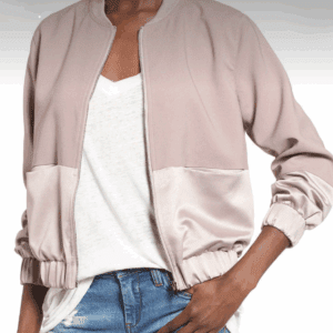 A person wearing a light mauve bomber jacket over a white V-neck T-shirt and blue jeans, standing with one hand on their hip.
