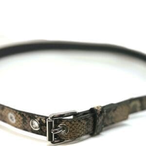 The Snake Skin Belt features a snake-patterned leather design with a silver buckle and metal eyelets, shown on a white background.