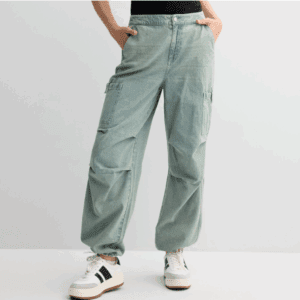 Person wearing Juniors High-Rise Elastic Cargo Jeans in light blue with side pockets, paired with white sneakers with black stripes and a black top, standing against a plain light background.