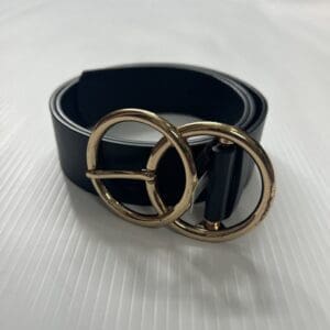 The Faux Leather Belt, featuring a gold double ring buckle, is rolled up and displayed on a textured white surface.