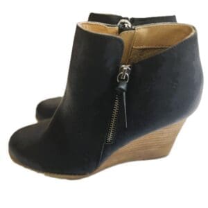A pair of black wedge ankle boots with side zippers and tan interior lining, featuring a wooden-look heel.