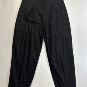 A pair of black pleated pants with a button and zipper closure, laid flat on a white surface.
