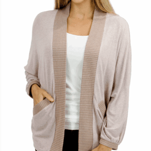 Woman wearing a light pink cardigan with ribbed trim, white top, and blue jeans, smiling with one hand in a pocket.