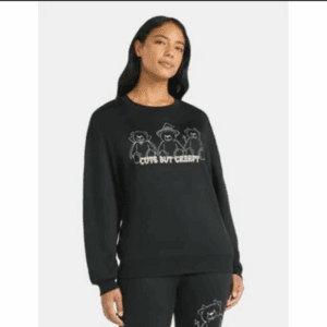 Woman wearing a black sweatshirt with line drawings of three cartoon cats and the text "Cute But Creepy" on the front.