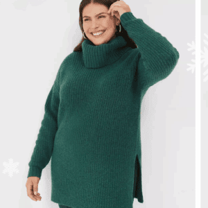 A woman wearing a Thick Ribbed Turtle Neck Sweater and dark jeans stands against a white background, smiling and touching her hair.