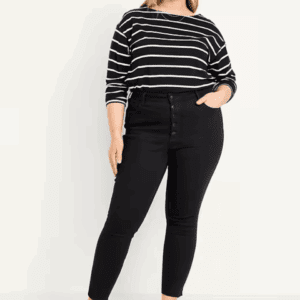 A person stands with one hand in their pocket, wearing a black and white striped long-sleeve top, high-waisted black skinny jeans, and a faux leather belt.